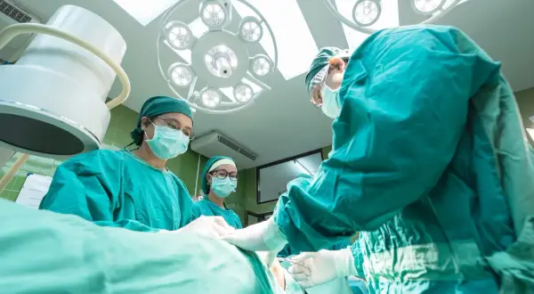 Zespół chirurgów w zielonych fartuchach i maskach przeprowadza operację nosa pod jasnym światłem lampy.